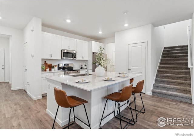 645 Flintwood Pl, Lafayette, CO 80026 - kitchen featuring stainless steel appliances, a breakfast bar area, white cabinets, light wood finished floors, and baseboards