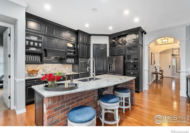 2038 Vineyard Dr, Windsor, CO 80550 - kitchen with high quality fridge, arched walkways, light wood-style floors, backsplash, and an island with sink