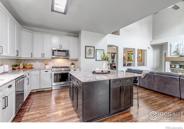 5111 Mt St Vrain Ave, Frederick, CO 80504 - kitchen featuring appliances with stainless steel finishes, open floor plan, dark wood-style flooring, a kitchen breakfast bar, and a high ceiling