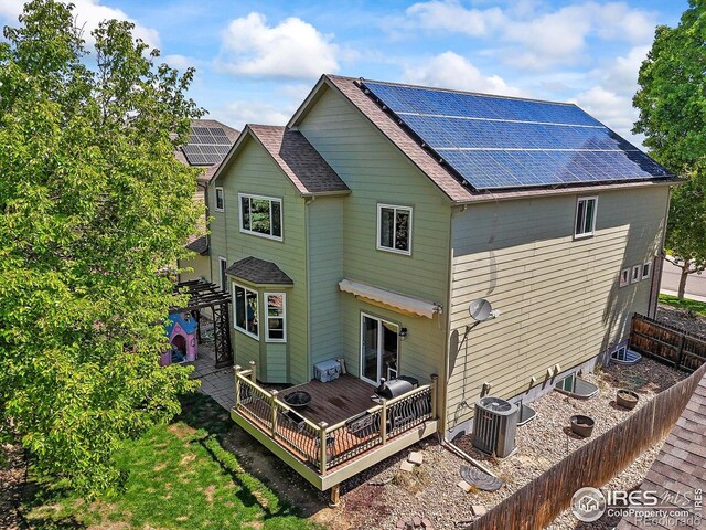 13445 Kearney St, Thornton, CO 80602 - back of house featuring cooling unit, solar panels, a fenced backyard, roof with shingles, and a wooden deck