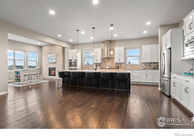 3075 Blue Mountain Dr, Broomfield, CO 80023 - kitchen with appliances with stainless steel finishes, wall chimney exhaust hood, a kitchen bar, dark wood-style flooring, and recessed lighting
