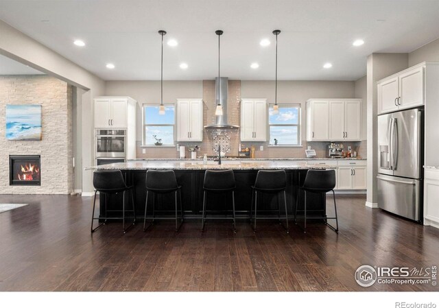 3075 Blue Mountain Dr, Broomfield, CO 80023 - kitchen with appliances with stainless steel finishes, wall chimney exhaust hood, dark wood-style flooring, an island with sink, and white cabinets