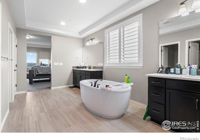 3075 Blue Mountain Dr, Broomfield, CO 80023 - ensuite bathroom with two vanities, a freestanding bath, wood finished floors, a tray ceiling, and recessed lighting