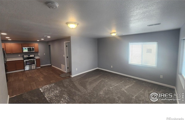 222 Platte St, Sterling, CO 80751 - unfurnished living room with baseboards, a textured ceiling, dark colored carpet, recessed lighting, and dark wood-style floors