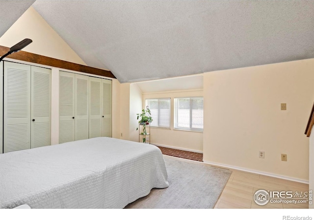 985 W 10th St Unit A5, Loveland, CO 80537 - bedroom featuring wood finished floors, vaulted ceiling, multiple closets, a textured ceiling, and baseboards