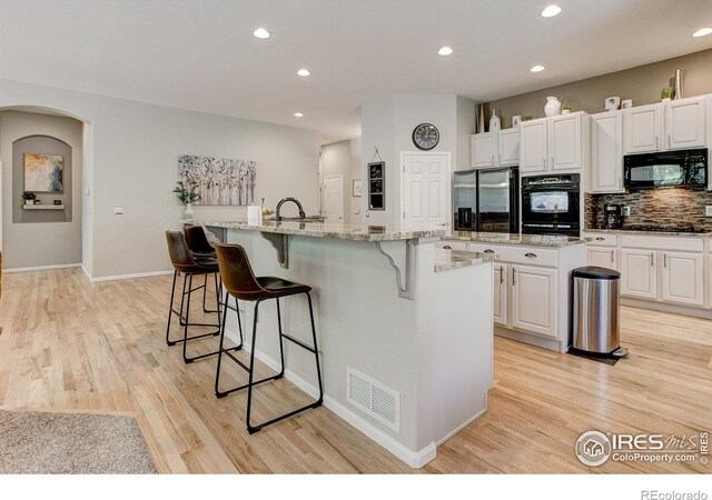 6208 Treestead Ct, Fort Collins, CO 80528 - kitchen featuring black appliances, an island with sink, a kitchen breakfast bar, light wood-style floors, and recessed lighting