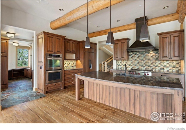409 Wild Horse Cir, Boulder, CO 80304 - kitchen featuring wall chimney range hood, double oven, beam ceiling, light wood finished floors, and backsplash