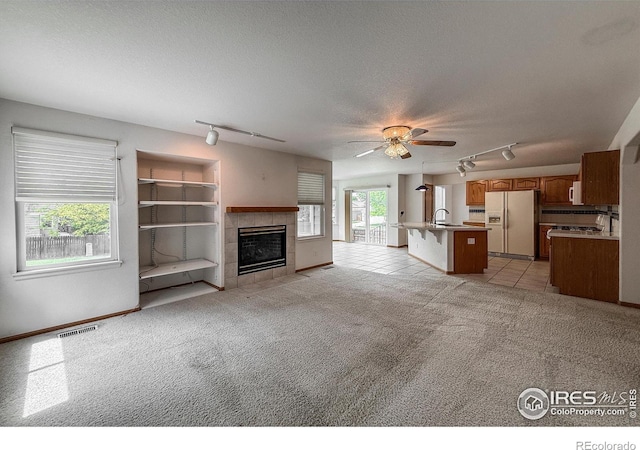 678 Mcclure Ct, Erie, CO 80516 - unfurnished living room with rail lighting, a sink, a fireplace, light carpet, and a textured ceiling