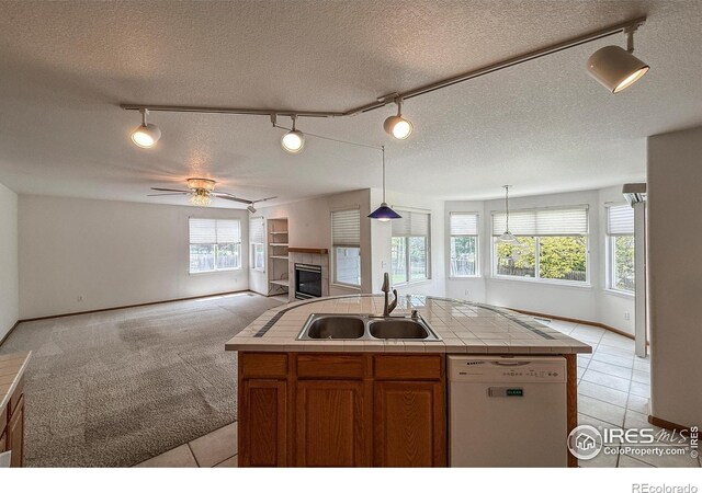 678 Mcclure Ct, Erie, CO 80516 - kitchen featuring white dishwasher, track lighting, a tiled fireplace, a sink, and open floor plan