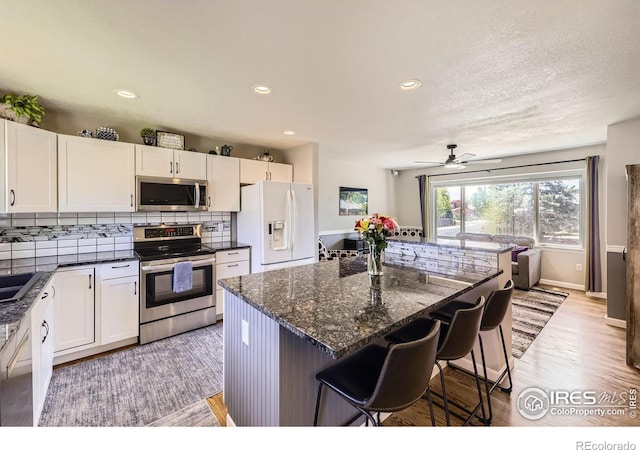 2447 E 100th Way, Thornton, CO 80229 - kitchen with appliances with stainless steel finishes, a breakfast bar area, white cabinets, tasteful backsplash, and recessed lighting