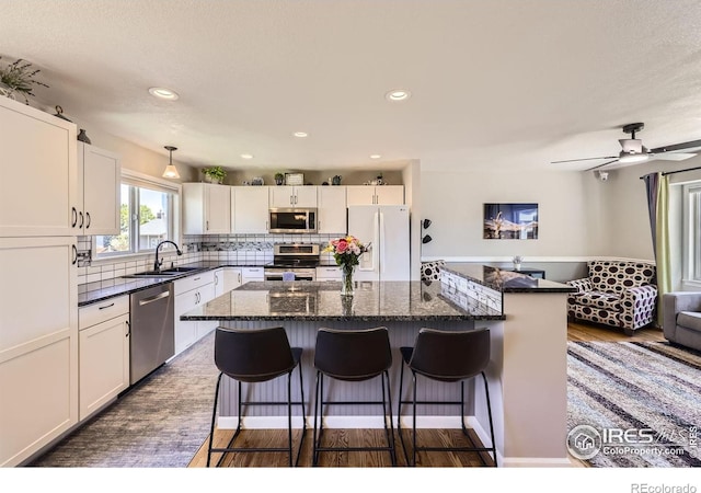 2447 E 100th Way, Thornton, CO 80229 - kitchen with appliances with stainless steel finishes, a sink, a kitchen breakfast bar, a kitchen island, and white cabinetry