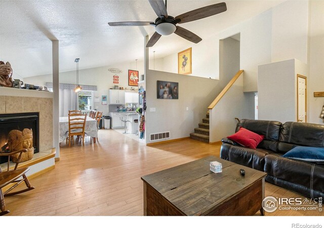 3328 Wild W Ln, Wellington, CO 80549 - living room featuring lofted ceiling, light wood finished floors, a ceiling fan, stairs, and a tile fireplace