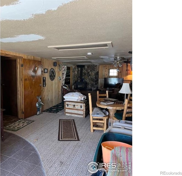 100 Santee Ct, Red Feather Lakes, CO 80545 - tiled living room with wood walls, a wood stove, a textured ceiling, and carpet flooring