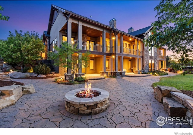 8236 County Road 74, Windsor, CO 80550 - back of property at dusk with a balcony, a fire pit, a patio area, stucco siding, and a chimney