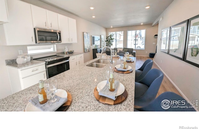 3356 Streamwood Dr, Johnstown, CO 80534 - kitchen with stainless steel appliances, wood finished floors, white cabinets, light stone countertops, and open floor plan