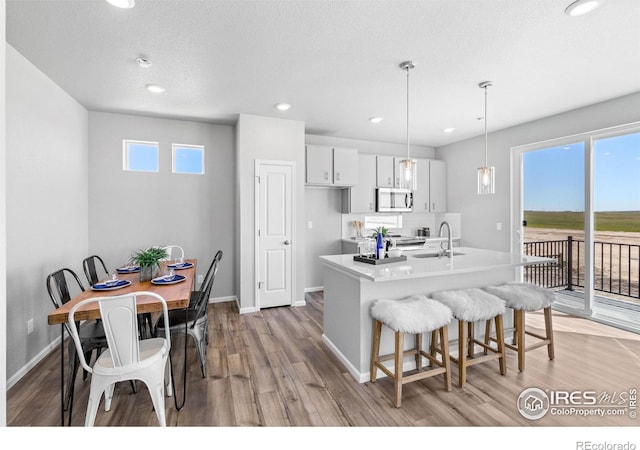 3364 Streamwood Dr, Johnstown, CO 80534 - kitchen featuring stainless steel microwave, light wood finished floors, a kitchen bar, white cabinetry, and hanging light fixtures