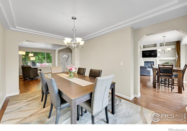 11740 Ivy St, Thornton, CO 80233 - dining area with a chandelier, a tray ceiling, arched walkways, light wood-type flooring, and a glass covered fireplace
