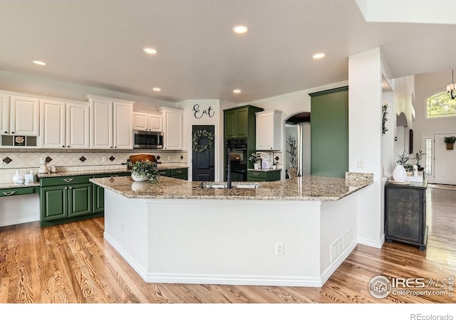 8839 Shetland Dr, Frederick, CO 80504 - kitchen featuring stainless steel microwave, arched walkways, green cabinetry, light wood-style flooring, and recessed lighting