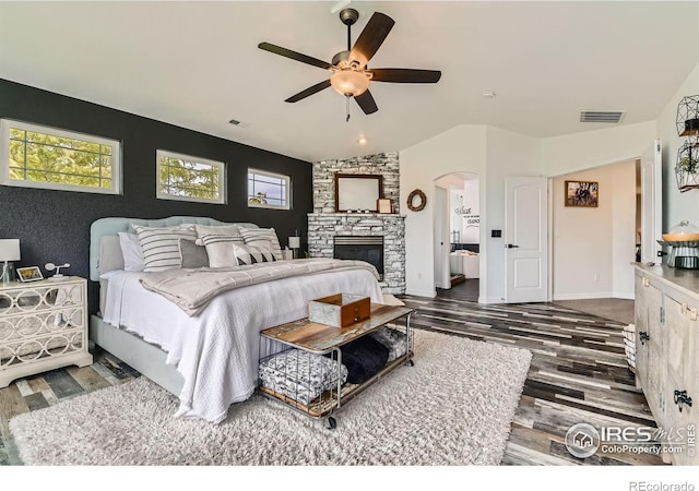 8839 Shetland Dr, Frederick, CO 80504 - bedroom with arched walkways, wood finished floors, a stone fireplace, vaulted ceiling, and ceiling fan