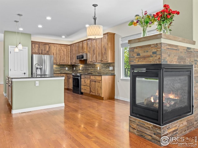 603 Summer Hawk Dr, Longmont, CO 80504 - kitchen featuring stainless steel appliances, dark countertops, a multi sided fireplace, light wood-type flooring, and brown cabinetry