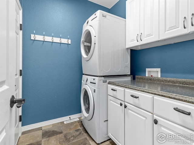 603 Summer Hawk Dr, Longmont, CO 80504 - washroom with stacked washer / dryer, baseboards, cabinet space, dark stone finish flooring, and a textured wall