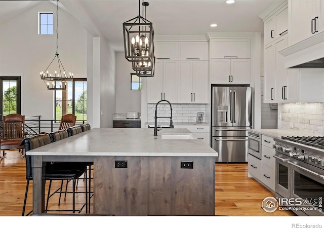 37179 Soaring Eagle Cir, Severance, CO 80550 - kitchen with appliances with stainless steel finishes, a chandelier, a breakfast bar, white cabinets, and light wood finished floors