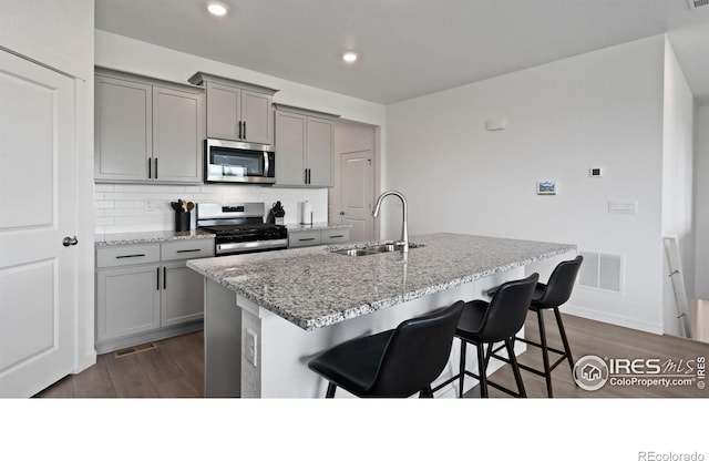 4709 Lynxes Way, Johnstown, CO 80534 - kitchen with stainless steel appliances, a sink, gray cabinetry, a breakfast bar, and dark wood-style floors