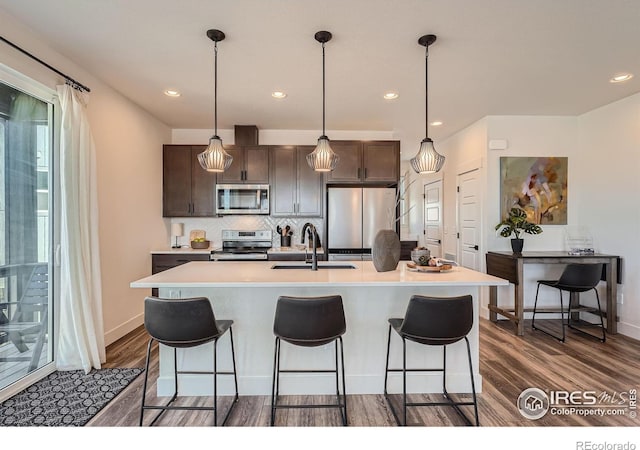 2446 W 167th Ln, Broomfield, CO 80023 - kitchen with appliances with stainless steel finishes, a sink, dark brown cabinetry, dark wood-style floors, and a kitchen breakfast bar