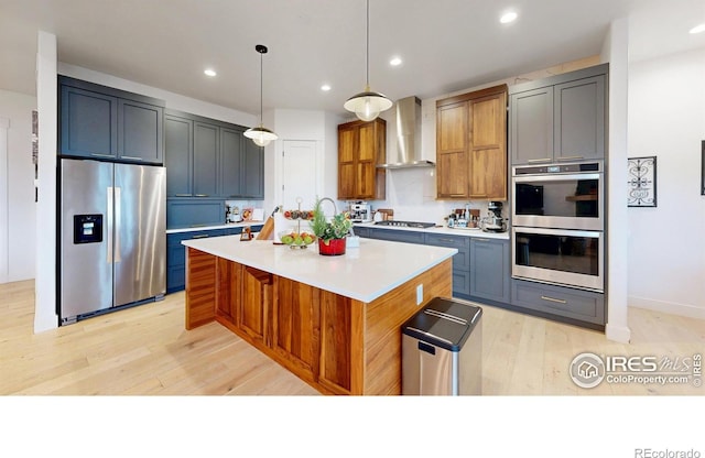 2790 Heron Lakes Pkwy, Berthoud, CO 80513 - kitchen with stainless steel appliances, wall chimney exhaust hood, light wood finished floors, light countertops, and an island with sink