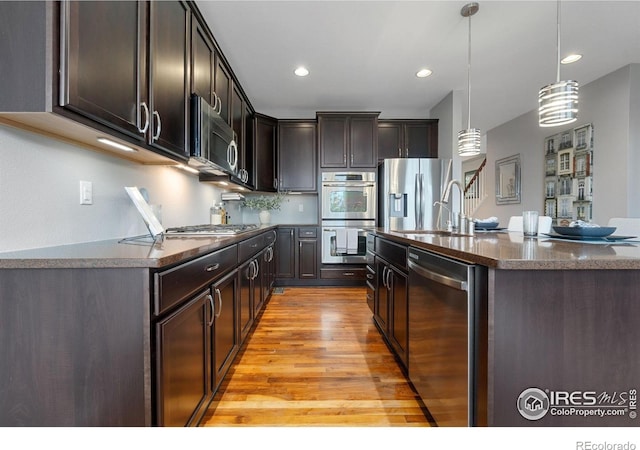 17805 Coral Burst St, Parker, CO 80134 - kitchen with appliances with stainless steel finishes, light wood finished floors, dark brown cabinetry, pendant lighting, and a center island with sink