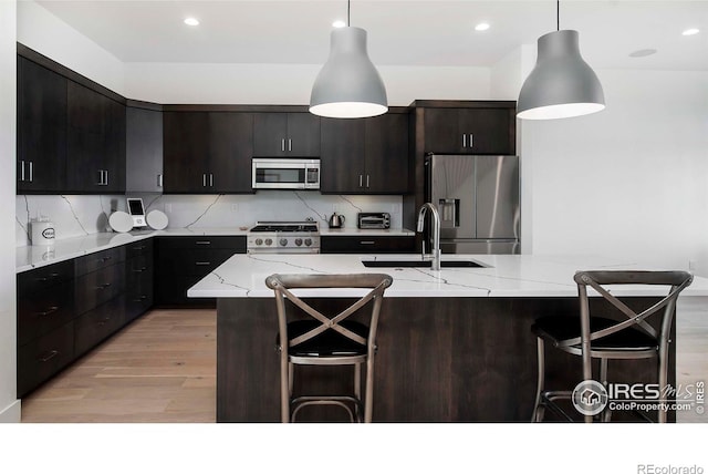 1769 Beachside Dr, Windsor, CO 80550 - kitchen featuring appliances with stainless steel finishes, a sink, light wood finished floors, a breakfast bar area, and a center island with sink