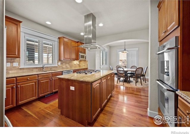 2005 Calico Ct, Longmont, CO 80503 - kitchen with arched walkways, a sink, appliances with stainless steel finishes, island range hood, and backsplash