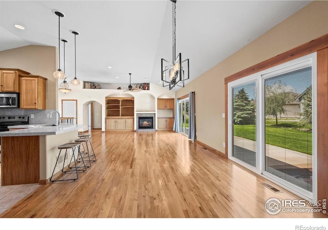 29 Pioneer Pl, Eaton, CO 80615 - kitchen featuring appliances with stainless steel finishes, high vaulted ceiling, a kitchen breakfast bar, brown cabinetry, and light wood-style floors