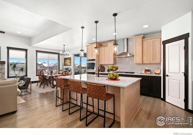 4521 Devereux Dr, Windsor, CO 80550 - kitchen featuring wall chimney exhaust hood, light brown cabinetry, light wood-style flooring, a breakfast bar, and recessed lighting