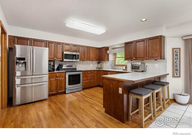 806 51st Ave, Greeley, CO 80634 - kitchen featuring appliances with stainless steel finishes, a peninsula, a kitchen bar, backsplash, and recessed lighting
