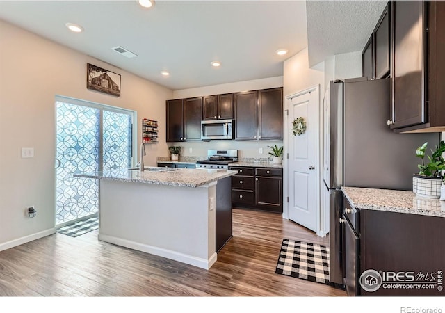 10 N Quantock St, Aurora, CO 80018 - kitchen featuring stainless steel appliances, wood finished floors, dark brown cabinetry, an island with sink, and recessed lighting