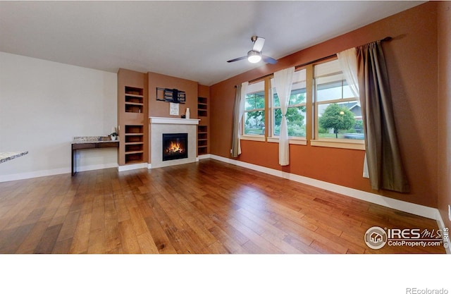 2107 Blackbird Dr, Fort Collins, CO 80525 - unfurnished living room featuring hardwood / wood-style floors, a ceiling fan, a glass covered fireplace, and built in shelves