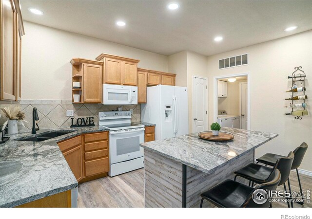 5551 29th St, Greeley, CO 80634 - kitchen featuring white appliances, a sink, a kitchen breakfast bar, light wood-style floors, and washing machine and clothes dryer