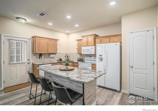 5551 29th St, Greeley, CO 80634 - kitchen featuring white appliances, decorative backsplash, light wood-style floors, a breakfast bar, and light stone countertops
