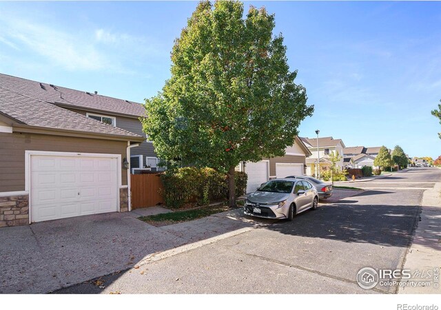 5551 29th St, Greeley, CO 80634 - view of property hidden behind natural elements with a residential view, stone siding, roof with shingles, a garage, and driveway