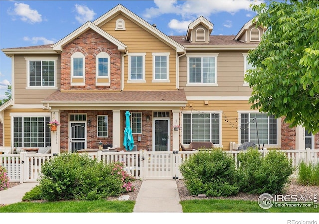 16031 W 63rd Ln W Unit D, Arvada, CO 80403 - view of front of home featuring covered porch, a fenced front yard, a gate, and brick siding