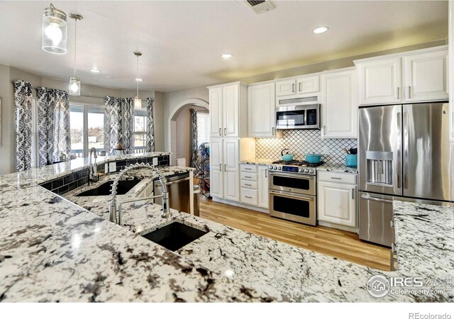 5895 E Conservation Dr, Frederick, CO 80504 - kitchen featuring appliances with stainless steel finishes, arched walkways, a sink, light stone countertops, and recessed lighting