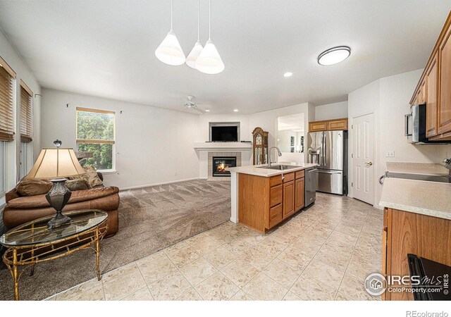 1874 Ute Creek Dr, Longmont, CO 80504 - kitchen featuring appliances with stainless steel finishes, open floor plan, a sink, a tiled fireplace, and brown cabinets