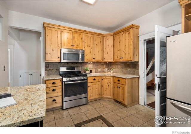 729 Peterson St, Fort Collins, CO 80524 - kitchen featuring appliances with stainless steel finishes, decorative backsplash, light tile patterned floors, and light stone counters