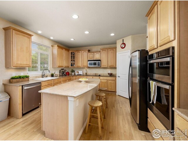 14246 Piney River Rd, Broomfield, CO 80023 - kitchen featuring stainless steel appliances, a center island, light brown cabinetry, a kitchen breakfast bar, and a sink