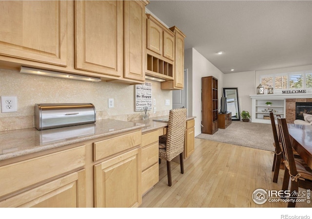 14246 Piney River Rd, Broomfield, CO 80023 - kitchen with light brown cabinetry, light wood finished floors, a tiled fireplace, open floor plan, and recessed lighting