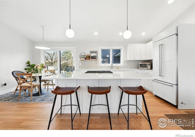 1670 Linden Ave, Boulder, CO 80304 - kitchen with stainless steel microwave, paneled refrigerator, light wood-style flooring, a breakfast bar area, and vaulted ceiling