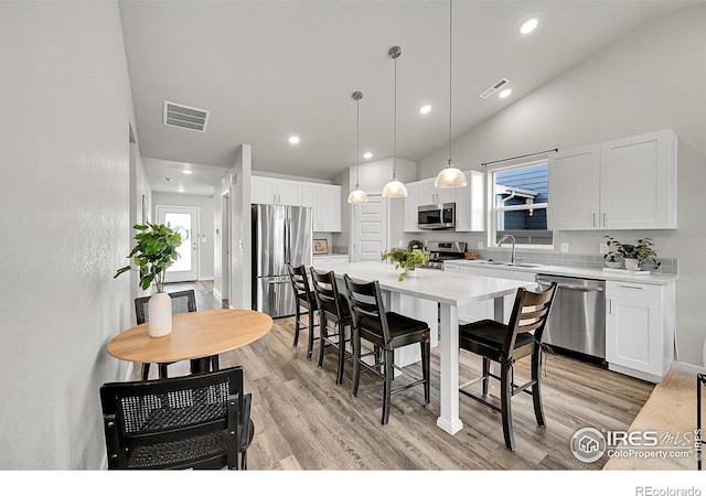 403 Pony Express Trl, Ault, CO 80610 - kitchen featuring appliances with stainless steel finishes, a kitchen breakfast bar, white cabinetry, light wood-type flooring, and lofted ceiling