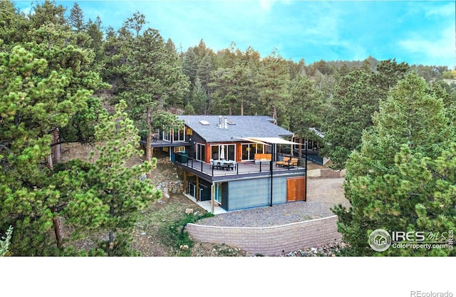279 Green Meadow Ln, Boulder, CO 80302 - back of property with a forest view, a deck, a garage, and a shingled roof