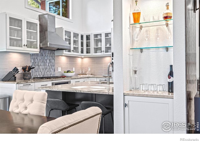 279 Green Meadow Ln, Boulder, CO 80302 - kitchen with wall chimney exhaust hood, decorative backsplash, white cabinets, stainless steel gas cooktop, and a breakfast bar